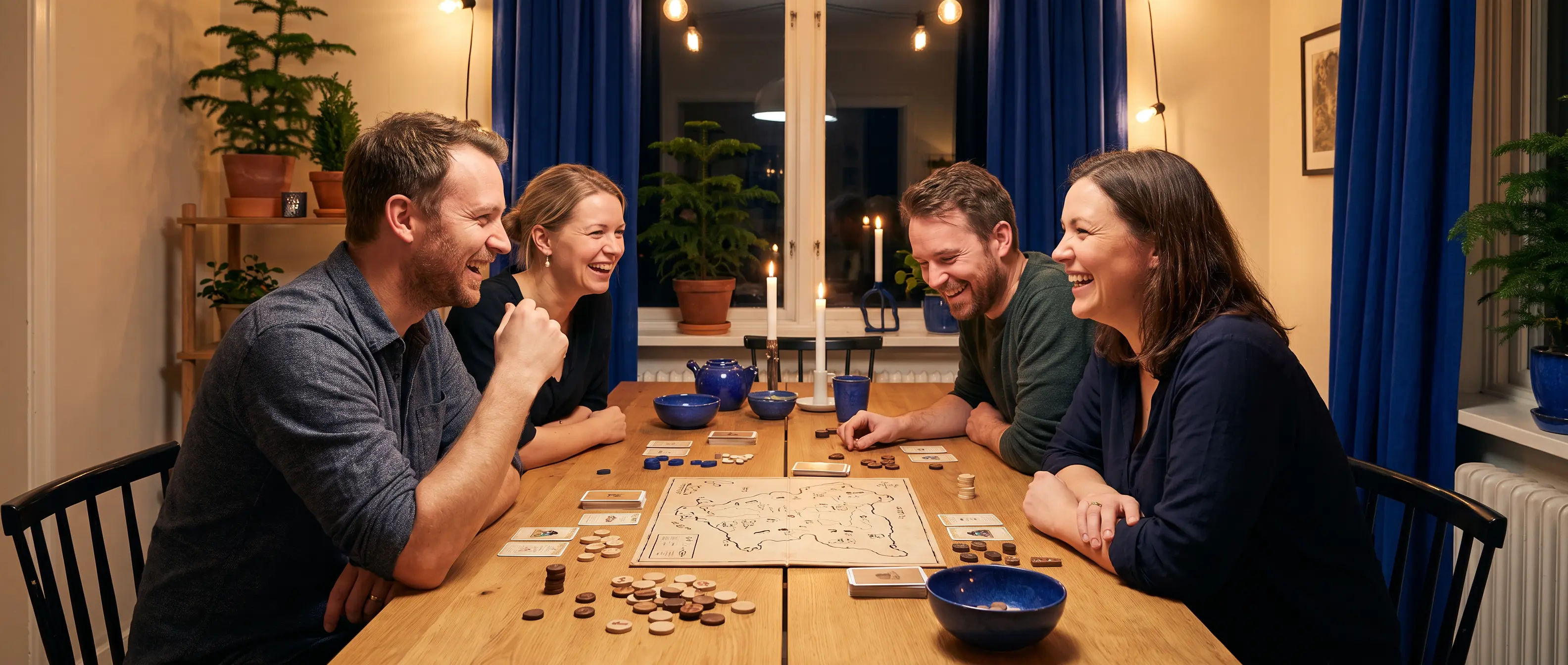 Four adults enjoying a tabletop game at a long table in the evening
